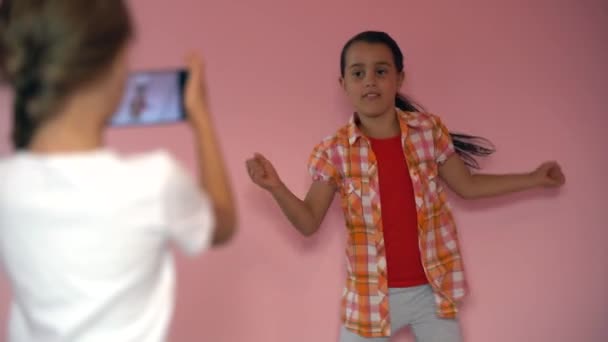 Kinder fotografieren mit dem Handy auf rosa Hintergrund. Nahaufnahme von Freunden beim Selfie auf dem Smartphone. - Filmmaterial, Video