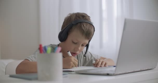 Junge hört Musik per Kopfhörer mit Laptop und zeichnet Bilder, sitzt zu Hause am Tisch - Filmmaterial, Video