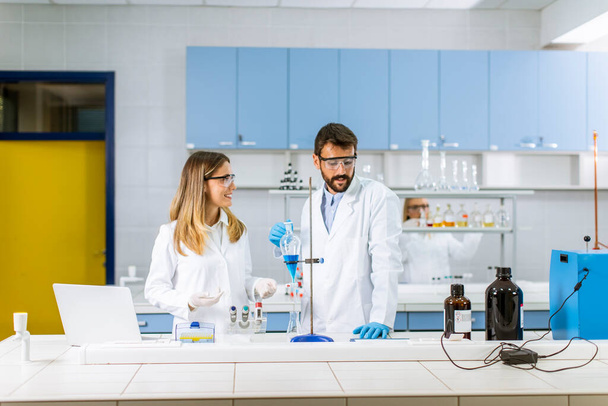 Исследователи, работающие с голубой жидкостью в сепараторной воронке в лаборатории - Фото, изображение