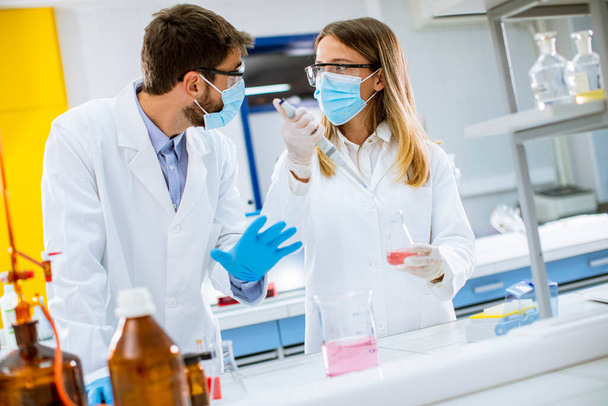 Ärztin mit Mundschutz und Schutzbrille im Labor hält Nadelspritze und Medikamentenflasche in der Hand - Foto, Bild