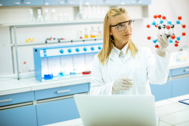 Female chemist with safety goggles hold molecular model in the lab - Photo, Image