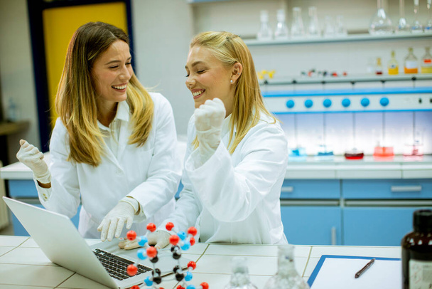 Investigadoras lindas en bata de laboratorio blanca usando portátil mientras trabajan en el laboratorio - Foto, imagen