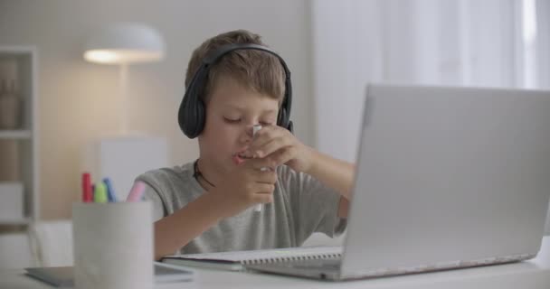 koulupoika piirtää kotona ja puhuu internetissä ystävän kanssa, käyttää kannettavaa tietokonetta ja kuulokkeita mikrofonilla - Materiaali, video