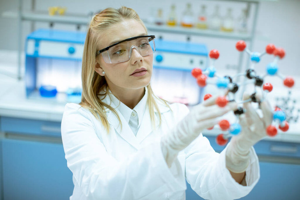 Női kémikus biztonsági védőszemüveggel tartsa molekuláris modell a laborban - Fotó, kép