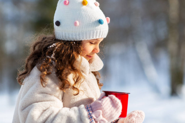 little girl with cup of hot tea in winter park - Fotó, kép