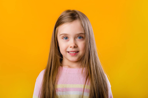 Portrait of a smiling little girl with long hair isolated on yellow background with  space for text - Valokuva, kuva