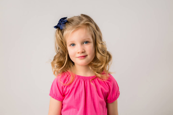Πορτρέτο ενός μικρού ξανθού κοριτσιού με μπούκλες σε ροζ t-shirt σε μπεζ φόντο - Φωτογραφία, εικόνα