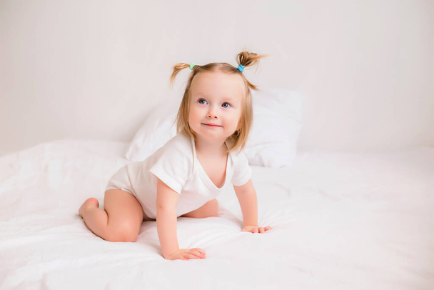 Photo of cute baby girl in white clothes lying on a bed and smiling - Photo, Image