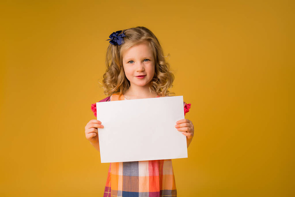Photo d'une fille tenant une feuille blanche vierge sur fond jaune. Copier l'image de l'espace avec placement pour votre texte de publicité - Photo, image