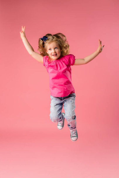 Nettes kleines blondes Mädchen in rosa T-Shirt und Jeans auf rosa Hintergrund. Leerzeichen-Bild mit Platzierung für Ihren Text oder Ihre Anzeige kopieren  - Foto, Bild