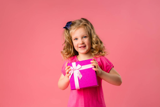 Copy space photo of a little cheerful girl with a gift box on a pink background - 写真・画像
