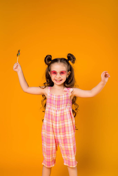 Cheerful girl with a lollipop on a yellow background. Copy space picture with placement for your text or advertisement - Fotó, kép