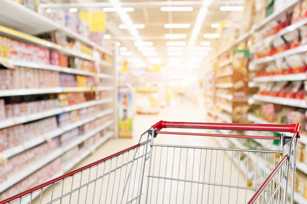 Empty shopping cart with abstract blur supermarket discount store aisle and product shelves interior defocused background - Foto, imagen