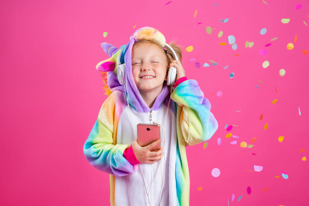 Menina loira feliz em unicórnio unitard escuta música de seu smartphone. Isolado em fundo rosa com um espaço para texto - Foto, Imagem