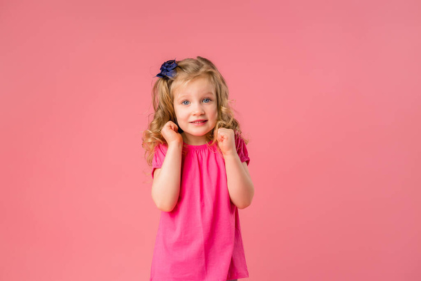 Schattig blond meisje in roze t-shirt op roze achtergrond. Kopieer ruimte foto met plaatsing voor uw tekst of advertentie. Begrip "emoties van kinderen" - Foto, afbeelding