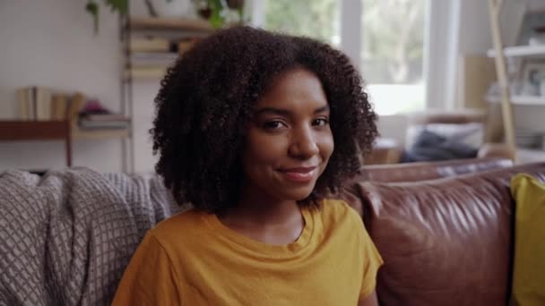 Portrait of happy african young woman sitting in living room smiling and looking at camera and laughing - Imágenes, Vídeo