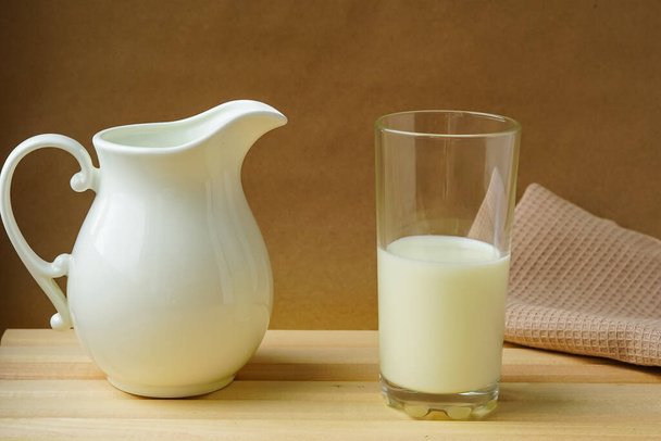 On a light wooden table lies a natural cotton napkin, there is a white milk jug and a glass with milk. Everything is ready for proper nutrition, healthy breakfast. Health First - Foto, immagini