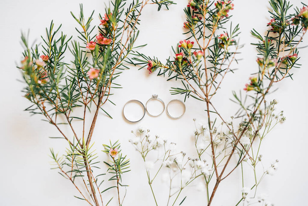 Обручальные кольца для молодоженов и обручальное кольцо невесты на белом фоне с белыми и красными цветами на ветках. - Фото, изображение