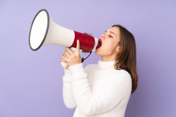 Teenager girl isolated on purple background shouting through a megaphone - Photo, Image