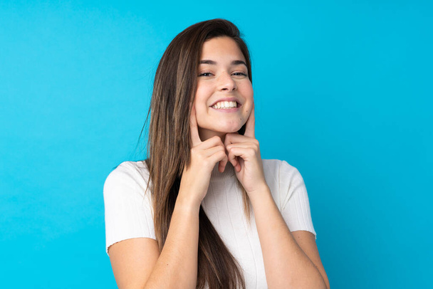 Teenager girl over isolated blue background smiling with a happy and pleasant expression - 写真・画像