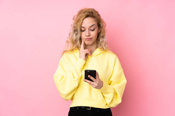 jonge blonde vrouw het dragen van een sweater geïsoleerd op roze achtergrond denken en het verzenden van een bericht - Foto, afbeelding