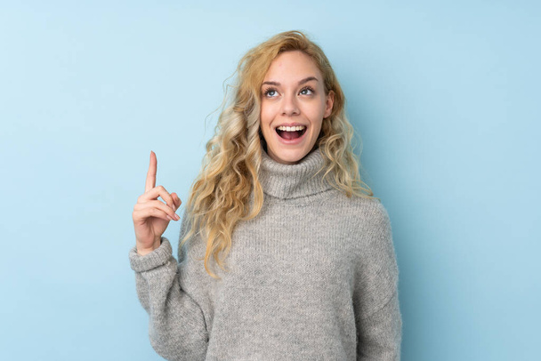 Young blonde woman wearing a sweater isolated on blue background pointing up and surprised - Photo, Image