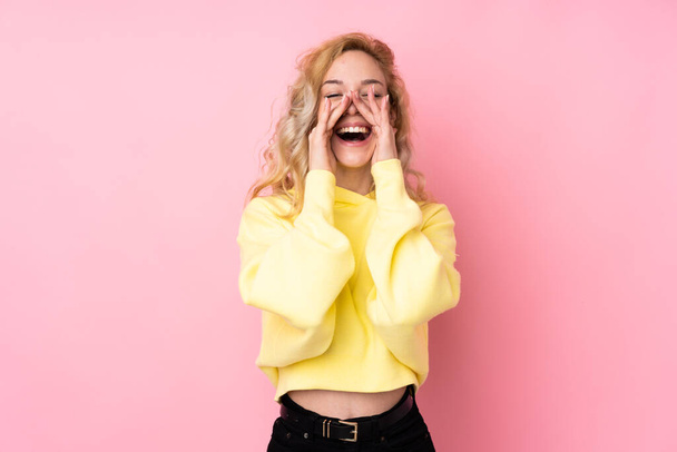 Young blonde woman wearing a sweatshirt isolated on pink background shouting and announcing something - Фото, зображення