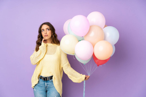 jonge vrouw vangen veel ballonnen over geïsoleerd op paarse achtergrond denken een idee - Foto, afbeelding