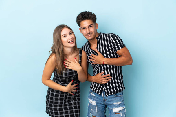 Teenager caucasian couple isolated on blue background smiling a lot while putting hands on chest - Foto, Bild