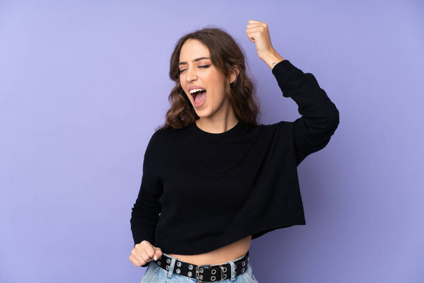 Young woman over isolated purple background celebrating a victory - Fotografie, Obrázek