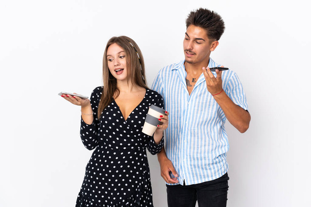 Jovem casal caucasiano isolado em fundo branco enviando uma mensagem de voz ou e-mail com o celular - Foto, Imagem