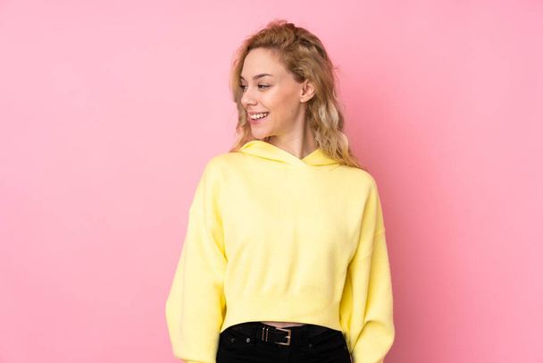 Young blonde woman wearing a sweatshirt isolated on pink background looking side - Foto, imagen