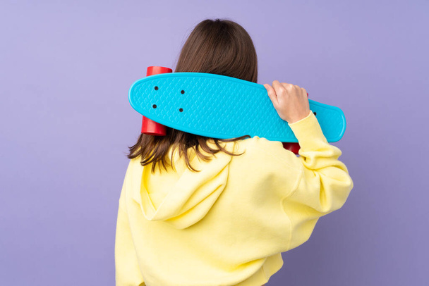 Teenager girl isolated on purple background with a skate in back position - Photo, Image