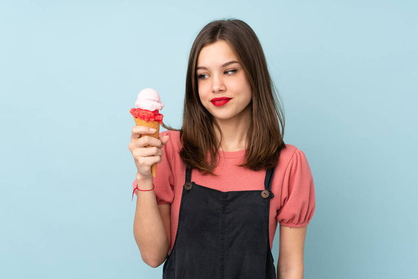 Teenager girl holding a cornet ice cream isolated on blue background with happy expression - Foto, Bild