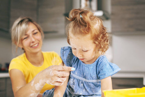 Una bambina vestita di blu, ricoperta di farina, guarda la mano di sua madre. Sfondo sfocato - Foto, immagini