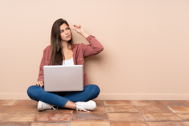 Teenager student girl sitting on the floor with a laptop making the gesture of madness putting finger on the head - Φωτογραφία, εικόνα