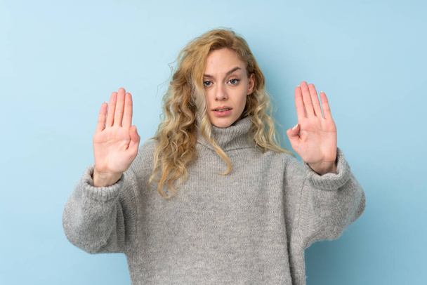 Junge blonde Frau trägt einen Pullover isoliert auf blauem Hintergrund macht Stop-Geste und enttäuscht - Foto, Bild