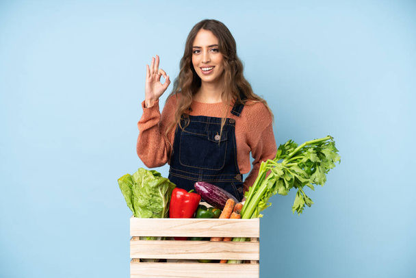 Фермер со свежими овощами в коробке показывает знак ОК с пальцами - Фото, изображение