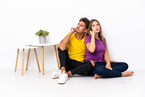 Young couple sitting on the floor isolated on white background thinking an idea while scratching head - Foto, imagen