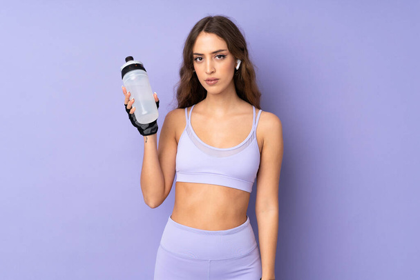 Young sport woman over isolated purple background with sports water bottle - Foto, Bild