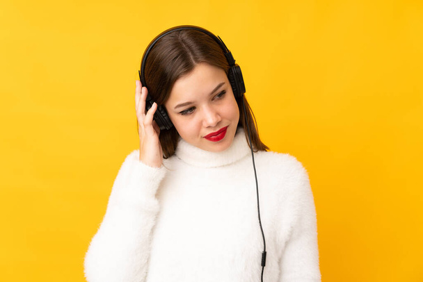 Teenager girl isolated on yellow background listening music - 写真・画像