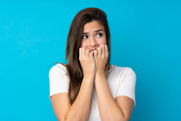 Adolescente menina sobre isolado azul fundo nervoso e assustado colocando as mãos na boca - Foto, Imagem