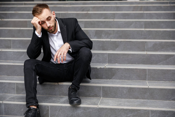 desperate young man in formal suit sitting on stairs - 写真・画像