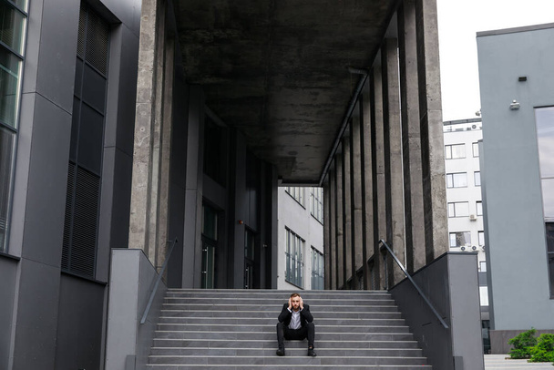 відчайдушний молодий чоловік в офіційному костюмі сидить на сходах
 - Фото, зображення