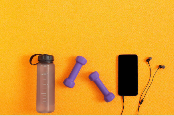 Miniatury, láhev s vodou a sluchátka na pozadí oranžové fitness rohože. Plochá kompozice. Koncept sportu, fitness, zdravého životního stylu. Horní pohled. Kopírovat prostor. - Fotografie, Obrázek