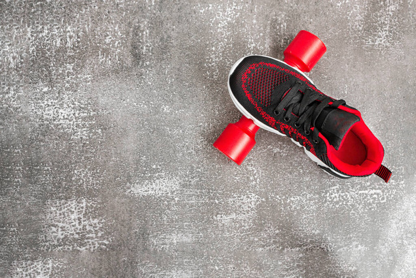 Black sneaker and red dumbbell on gray background. Concept of sport, fitness, healthy lifestyle. Copy space, flat lay. - Zdjęcie, obraz