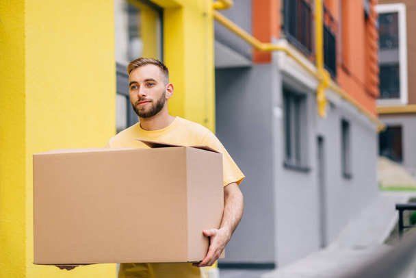 delivery worker wearing yellow t-shirt holding box - Fotó, kép