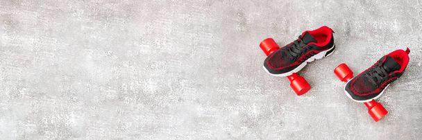 Ein Paar neue schwarze Turnschuhe und rote Hanteln auf grauem Hintergrund. Konzept von Sport, Fitness, gesundem Lebensstil. Banner. Kopierraum. - Foto, Bild