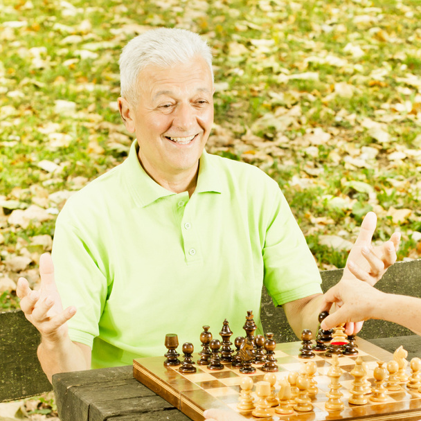 szczęśliwy człowiek starszy, gra w szachy na ławce w parku - Zdjęcie, obraz