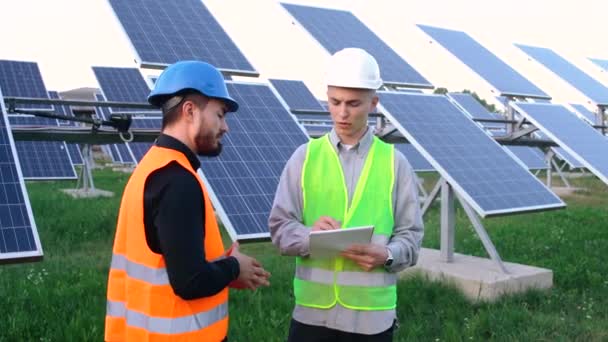 Un ingeniero senior con un plan de instalación de paneles solares explica a un trabajador cómo hacerlo - Imágenes, Vídeo